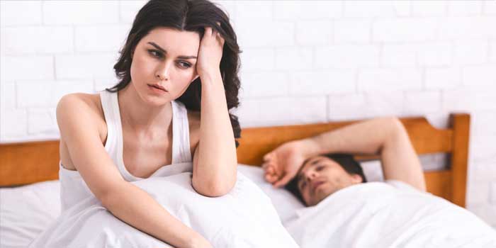 男性が寝ている横で頭を抑え悩む様子の女性